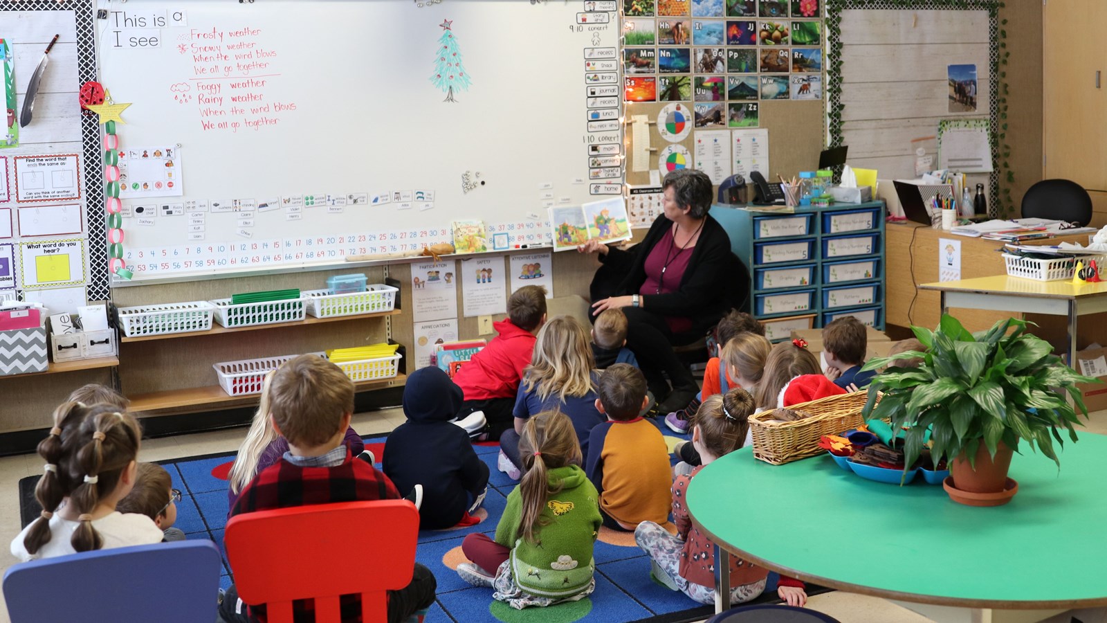 Kindergarten students sit and listen to a book being read by their teacher.